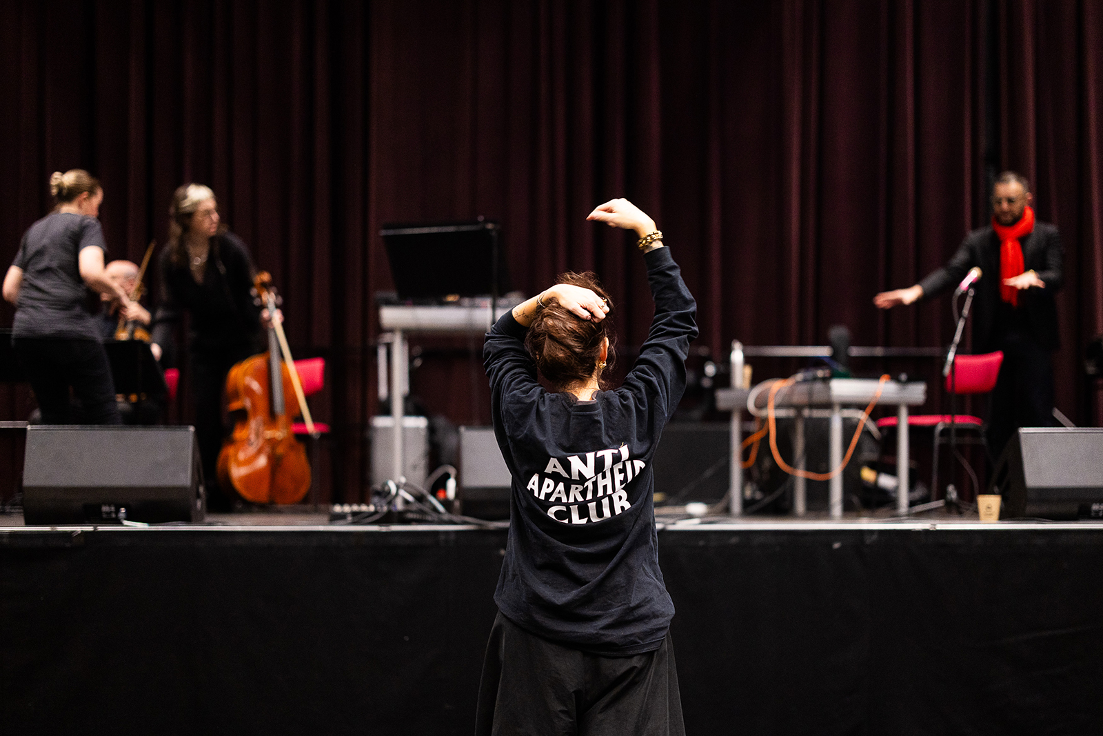 Musicians are setting up on stage. In front, Liliane Chlela is standing with a sweater that says 'anti apartheid club'